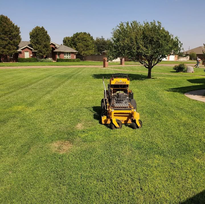 Yellow stand-on mower on a wide green lawn
